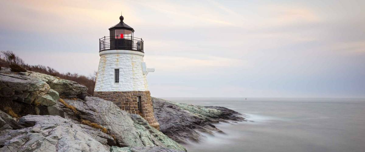 Small, white, granite built Castle Hill Lighthouse sits on the rocky coastline of Newport, Rhode Island