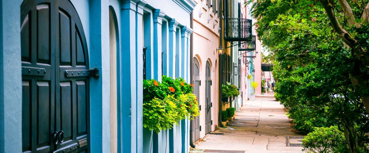 Empty sidewalk view of lush summer greenery lining the colorful Georgian architecture of the colonial Rainbow Row in the historical Battery neighborhood of Charleston, South Carolina, USA